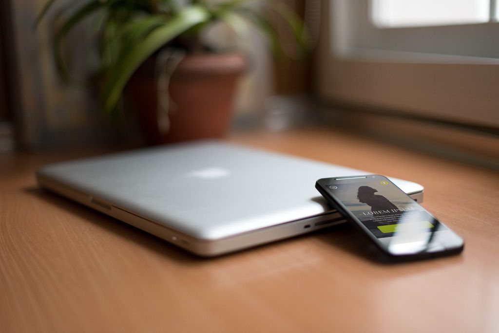 Close-up of a silver laptop and smartphone on a wooden desk, capturing modern work essentials.